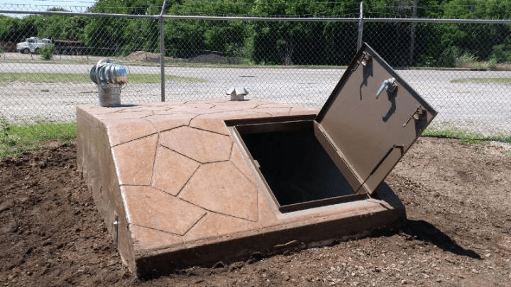 A concrete storm shelter sits partially underground in a rural Oklahoma